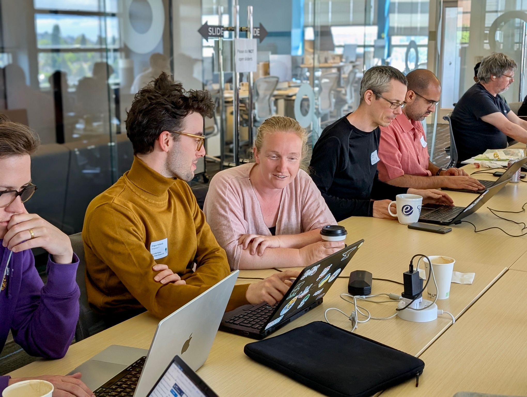 Photograph of Angus and Franklin co-working with Scientific Python developers during the summit. Image redistributed from a LinkedIn post shared by Scientific Python.