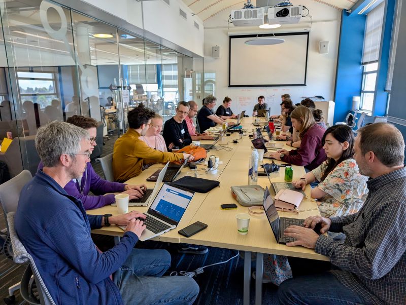 Photograph of Angus and Franklin co-working with Scientific Python developers during the summit. Image redistributed from a LinkedIn post shared by Scientific Python.